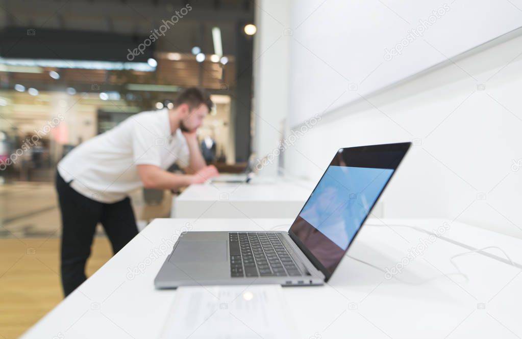 Laptop is in the shop window of electronics on the back of the buyer. Buy a laptop in a technology store. Focus on the laptop.