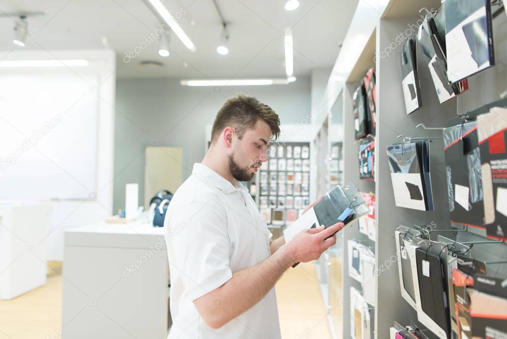 Man is in the electronics store and chooses accessories for gadgets. Purchasing accessories in the technology store.