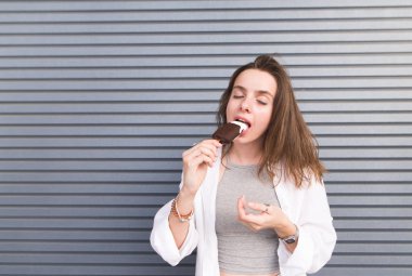 Güzel kız gözleri ile çikolatalı dondurma yeme gri bir arka plan üzerinde kapalı. Çekici bir kız çikolatalı dondurma yeme keyfini.
