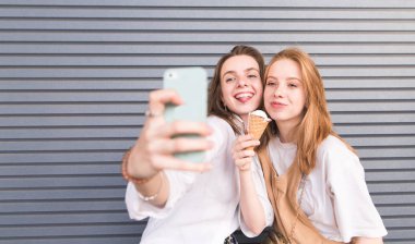 Selfie telefonu almak ışık yaz giysileri iki şık kadın portresi. İki güzel kız arkadaşım bir sephi gri bir duvar arka plan üzerinde almak..
