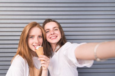 Parlak elbise sevimli mutlu genç kadınlarda selfie karanlık bir arka plan üzerinde olun. Çekici genç kız selfie arka plan gri duvarlar üzerinde dondurma ile yapıyor. Kız Smartphone'da fotoğraflandı