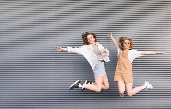 İki mutlu kız parlak yaz giysileri gri bir duvar arka plan üzerinde bak içine belgili tanımlık fotoğraf makinesi ve gülümseme atlamak. Koyu arka plan üzerinde atlama hareket gülümseyen moda kız portresi