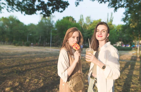 Две Привлекательные Девушки Парке Держат Руках Лимонад Леденцы Смотрят Камеру — стоковое фото