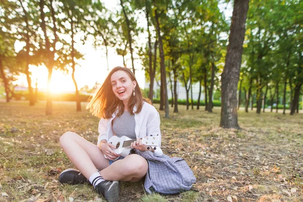 Sorrindo Menina Elegante Senta Parque Joga Ukulele Branco Olha Para — Fotografia de Stock