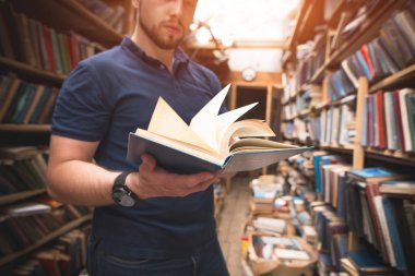 Açık bir kitap bir halk kütüphanesi arka plan elinde olan adam. Bir adam yakın çekim elinde kitaptır. Edebiyat kavramı. Kütüphanede kitap