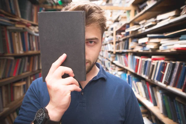 Портрет Студента Стоящего Библиотеке Закрывающего Лицо Черной Книгой Смотрящего Камеру — стоковое фото