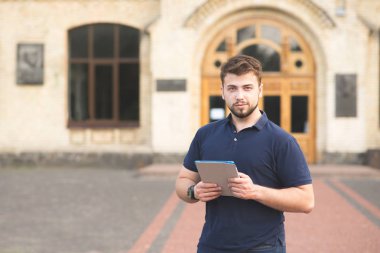 Binanın arka planı elinde bir tablet ile ayakta ve kameraya bakarak bir sakallı bir adam portresi. Öğrenci üniversite binasının arka planda bir tablet ile.
