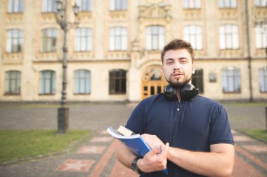 Portre binanın arka plan üzerinde duran ve kameraya bakarak onun elinde kitap olan bir adam. Onun elinde kitap olan öğrencinin kampüs Üniversitesi ve pozlar kameraya duruyor