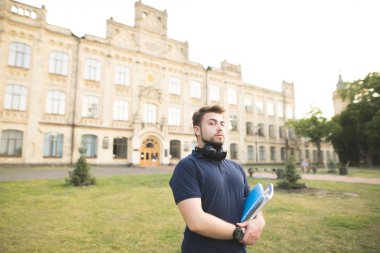 Elleri ve kameraya seyir ile bir kampüste bir sakal konumu olan bir adam portresi kitaplar. Öğrenci defter üzerinde üniversite arka plan ile. Kavram öğrenme