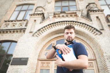 Eski üniversite binasının arka planı elinde kitap olan bir öğrenci portresi. Adam bir sakal ve onun elleri ayakları bir kitapta eski mimari arka plan üzerinde.