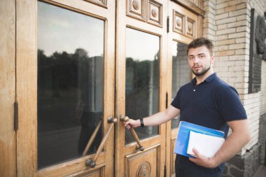 Kitaplar ve ellerini dizüstü bilgisayarlar ile öğrenci üniversite kapısını açar ve kameraya benziyor. Üniversite binası, sakallı bir kitaplar onun elinde ciddi adam bir parçasıdır.