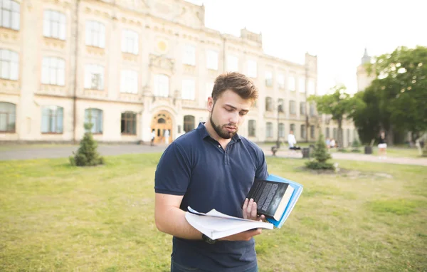 Sinirli adam sakallı bir kitaplar ile bir bina arka planı elinde duruyor. Üniversite binası arka plan karşı duran ve seyir defter üzgün öğrenci