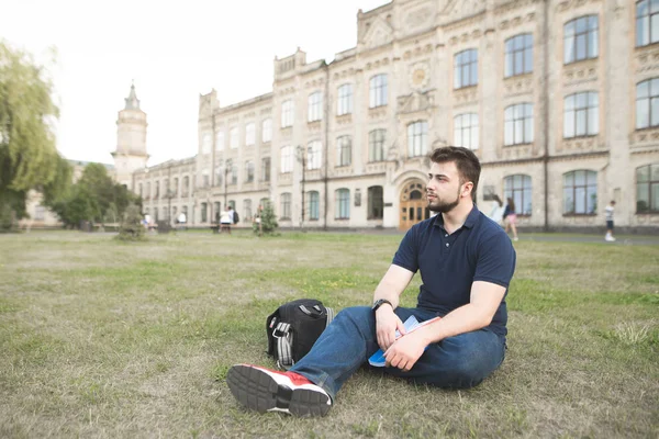 Bir üniversite kampüsünde bir çimenlikte oturan ve dinlenme öğrenci. Bir sakallı university yakınındaki çimenlerin üzerinde oturur ve yan görünüyor.