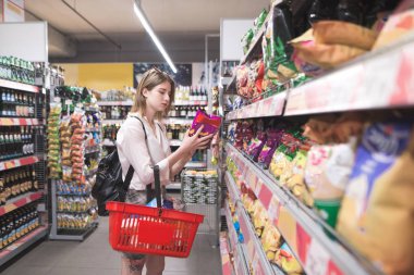 Kız onun elinde kırmızı bir sepet ile cips süpermarket raflarında seçer. Çekici genç kadın süpermarket Aperatif departmanında fiş satın alır. Bir süpermarket kavram alışveriş