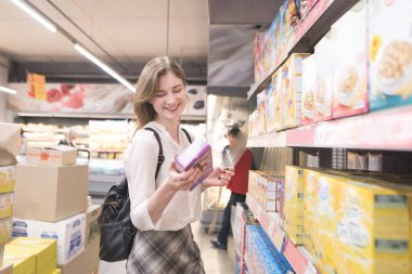 Bir paket içinde elleri ve gülümsüyor hızlı kahvaltı ile süpermarkette mutlu, çekici kadın var. Gülümseyen kız pul bir süpermarkette satın alır.