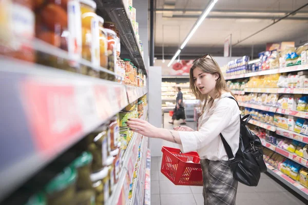 Stylish Young Woman Red Shopping Basket Her Hands Selects Canned — Stock Photo, Image