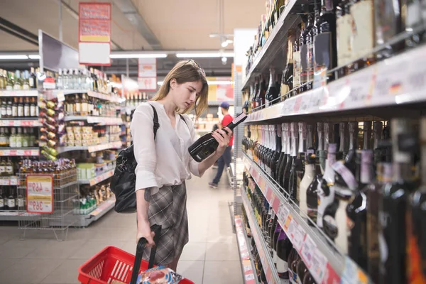 쇼핑백와 여자는 슈퍼마켓에서 알코올을 선택합니다 슈퍼마켓에서 제품의 선택입니다 저장소에서 — 스톡 사진