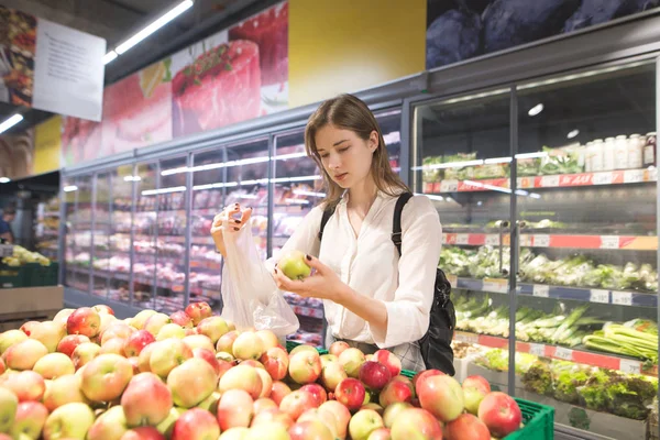 Genç çekici kadın elma meyve bölümü süpermarket satın alır. Güzel kız elma depoda seçer. Bir süpermarkette meyve alımı