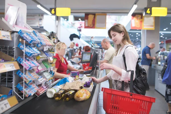Kız markette anlamına gelir ve bir sıra için bekler. Süpermarket'ın nakit masasında alımları için öder. El süpermarket ve satın ürünlerinde kasada duran kırmızı sepet ile gülümseyen kız