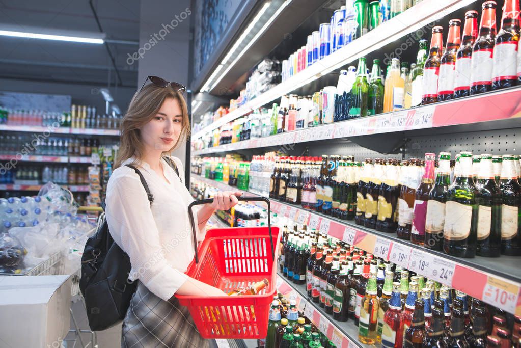 Portrait of an attractive girl from a supermarket at a beer department and looking at the camera. Woman with a jellyfish in her hands standing in the supermarket looking at the camera and smiling