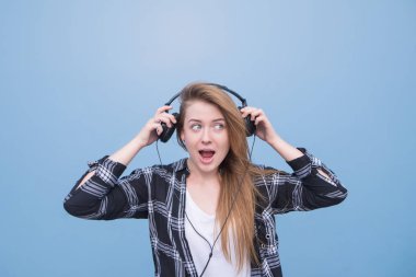 Kulaklıklar başını çeker bir duygusal çekici kız portresi. Kulaklık isiolated mavi bir arka plan üzerinde olumlu kızla