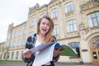 Duygusal öğrenci onun elinde açık bir kitap ile açık havada duruyor ve şaşkın bir bakışla kameraya benziyor. Arka bina Üniversitesi elinde bir defter ile duygusal kız öğrenci