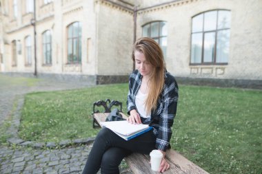 Açık havada üniversite kampüsünde sevimli kız öğrenci. Kız bir defter bir college yakınındaki bir bankta okur. Öğrenci kavramı