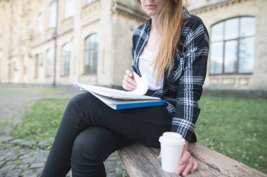 Bir fincan kahve, dizüstü bilgisayarlar ve bir kitap ile bir üniversite kampüsünde bir bankta oturmuş öğrenci. Öğrenci kavramı