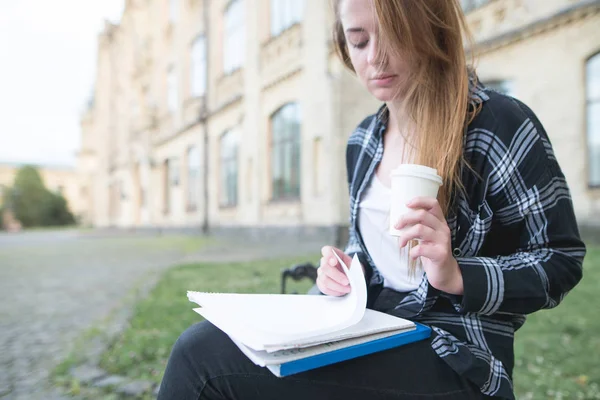 美丽的女生坐在一所大学背景的长凳上 读着笔记本 喝着咖啡 学生概念 休息时学习 — 图库照片