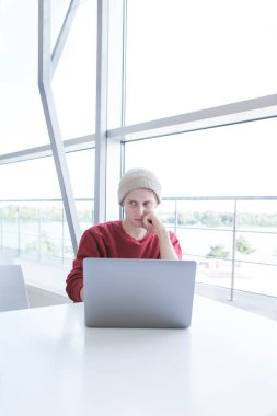 Genç şık freelancer adam pencerenin yakınındaki bir dizüstü bilgisayarda çalışıyor. Öğrenci ile modern bir iç ışık bir kafede bir dizüstü bilgisayar kullanarak. Genç bir işadamı portresi