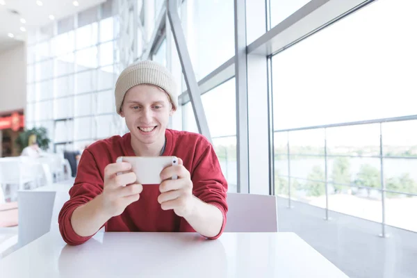 Усміхнений Молодий Чоловік Повсякденному Одязі Сидить Кафе Використовує Смартфон Позитивний — стокове фото
