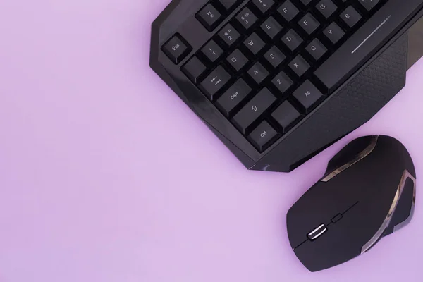 Black mouse and keyboard on a pink background, top view. Workplace, mouse and keyboard flat lay. Computer devices