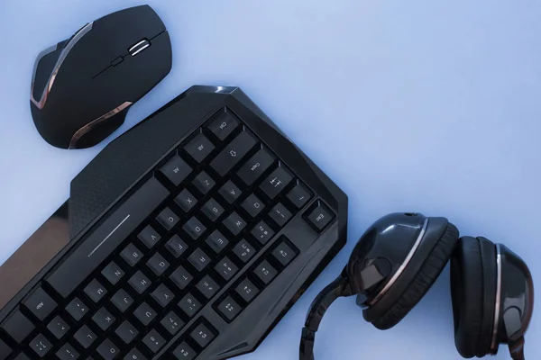 Headphones, mouse, keyboard on the blue background, top view. Gamer background. Computer devices, top view. Gaming gear. Gamer workspace