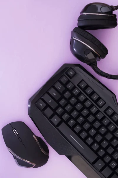 Headphones, mouse, keyboard on the pink background, top view. Gamer background. Computer devices, top view. Gaming gear. Gamer workspace