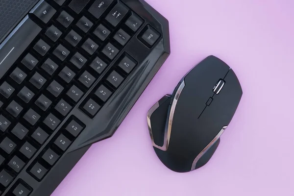 Black mouse and keyboard on a pink background, top view. Workplace, mouse and keyboard flat lay. Computer devices
