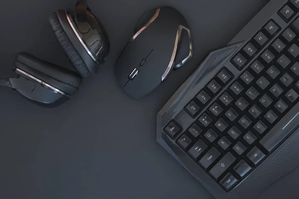 Black mouse, the keyboard, the headphones are isolated on a dark background, the top view. Flat lay gamer background. Workspace with a keyboard and mouse on a black background. Copyspace