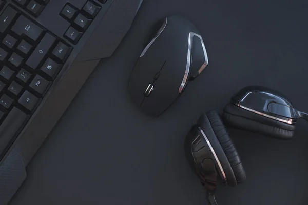 Black mouse, the keyboard, the headphones are isolated on a dark background, the top view. Flat lay gamer background. Workspace with a keyboard and mouse on a black background. Copyspace