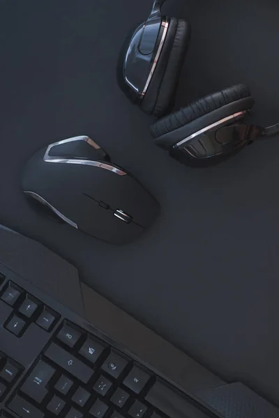 Black mouse, the keyboard, the headphones are isolated on a dark background, the top view. Flat lay gamer background. Workspace with a keyboard and mouse on a black background. Copyspace