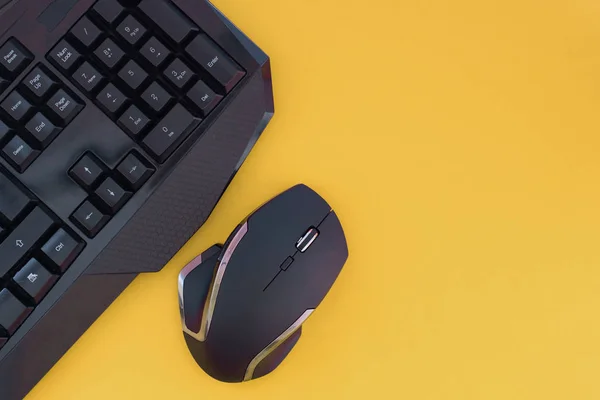 Black mouse, keyboard isolated on a yellow background, top view. Flat lay gamer background. Workspace with a keyboard and mouse on a yellow background. Copyspace