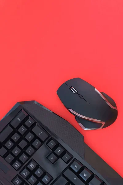 Black mouse, keyboard isolated on a red background, top view. Flat lay gamer background. Workspace with a keyboard and mouse on a black background. Copyspace