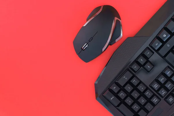 Black mouse, keyboard isolated on a red background, top view. Flat lay gamer background. Workspace with a keyboard and mouse on a red background. Copyspace