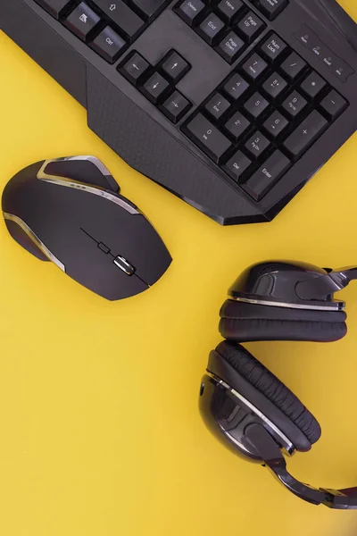 Black mouse, the keyboard, the headphones are isolated on a yellow background, the top view. Flat lay gamer background.Workplace with a keyboard, mouse and headphones on a yellow background. Copyspace