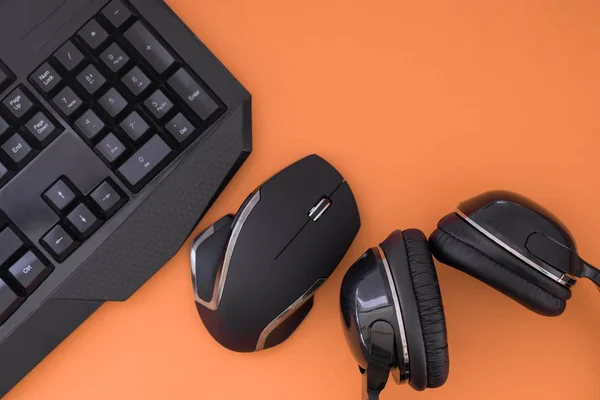 Flat lay gamer background. Mouse, the keyboard, the headphones are isolated on a orange background, the top view. Copyspace. Workspace with a keyboard and mouse on a orange background. Copyspace
