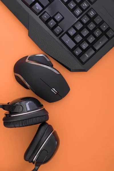Flat lay gamer background. Mouse, the keyboard, the headphones are isolated on a orange background, the top view. Copyspace. Workplace with a keyboard, mouse and headphones on a orange background.