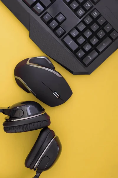 Flat lay gamer background. Mouse, the keyboard, the headphones are isolated on a yellow background, the top view. Copyspace. Workplace with a keyboard, mouse and headphones a yellow background.