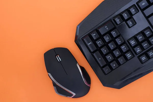 Workspace with a keyboard and mouse on a orange background. Copyspace. Black mouse, keyboard isolated on a orange background, top view. Flat lay gamer background. Copyspace