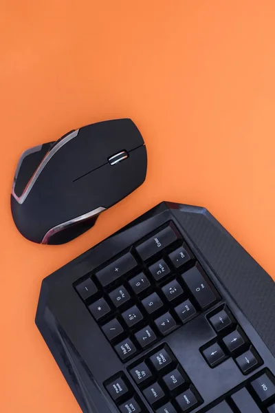 Workspace with a keyboard and mouse on a orange background. Copyspace. Black mouse, keyboard isolated on a orange background, top view. Flat lay gamer background.
