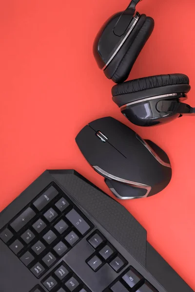 Flat lay gamer background. Mouse, the keyboard, the headphones are isolated on a red background, the top view. Copyspace. Workplace with a keyboard, mouse and headphones a red background.