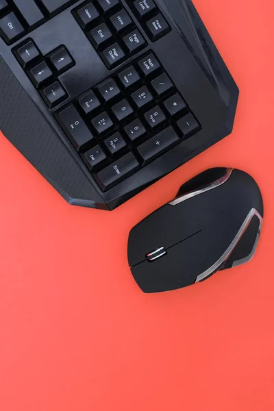 Workspace with a keyboard and mouse on a red background. Copyspace. Black mouse, keyboard isolated on a red background, top view. Flat lay gamer background. Copyspace