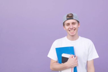 Onun elinde mor bir arka plan üzerinde izole bir defter ve Kitaplar ile mutlu öğrenci kamera ve gülümsüyor görünüyor. Sokak kitapları arka planını mor bir duvar ile genç bir adam portresi